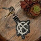 Close‑up of embroidered anarchy keychain with white stitching