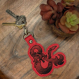Close‑up of embroidered D&D dragon ampersand keychain in red