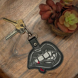 Close‑up of embroidered fangs on faux leather keychain with red accent