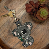 Close‑up of embroidered koala keychain holding a green leaf