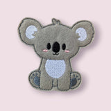 Handmade grey koala finger puppet displayed on a plain pale pink background. 