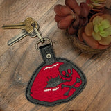 Close‑up of embroidered lips keychain with skull and crossbones design