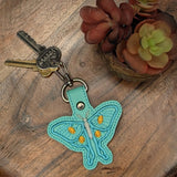 Close‑up of embroidered turquoise Luna Moth keychain with yellow details