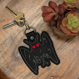 Close‑up of faux leather embroidered Mothman keychain with red eyes