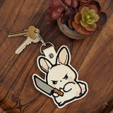 Faux leather embroidered Murder Bunny keyring holding knife on wooden tray