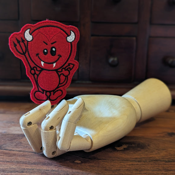Embroidered devil halloween finger puppet made from felt displayed on a wooden mannequin hand. 