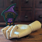 Embroidered witch halloween finger puppet made from felt displayed on a wooden mannequin hand. 