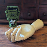 Embroidered Frankenstein halloween finger puppet made from felt displayed on a wooden mannequin hand. 