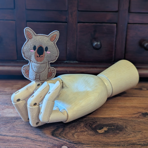 Embroidered wombat finger puppet made from felt displayed on a wooden mannequin hand. 