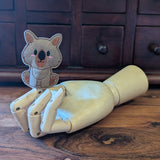 Embroidered wombat finger puppet made from felt displayed on a wooden mannequin hand. 