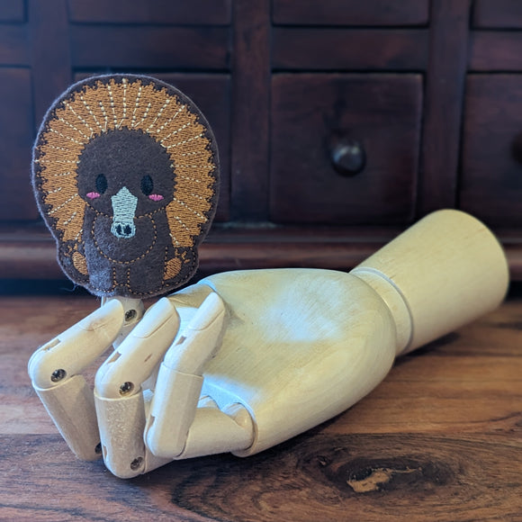 Embroidered echidna finger puppet made from felt displayed on a wooden mannequin hand. 