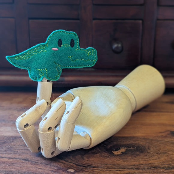 Embroidered crocodile finger puppet made from felt displayed on a wooden mannequin hand. 
