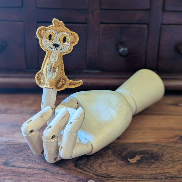 Embroidered meerkat finger puppet made from felt displayed on a wooden mannequin hand. 