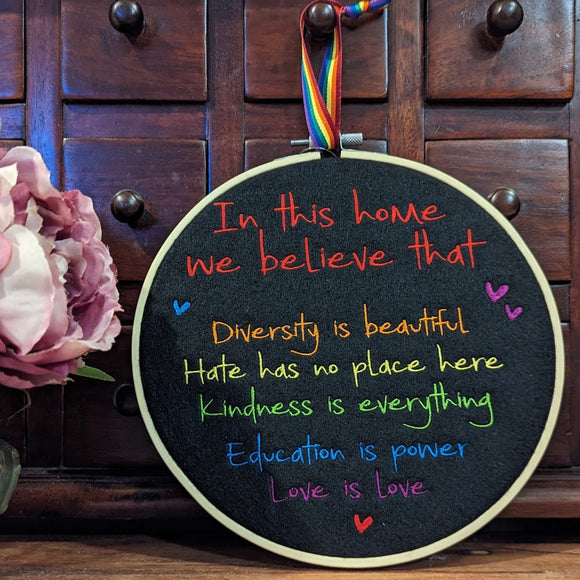 Machine embriodered text in rainbow colours on black felt that reads; in this home we believe that diversity is beautiful, hate has no place here, kindness is everything, education is power and love is love.