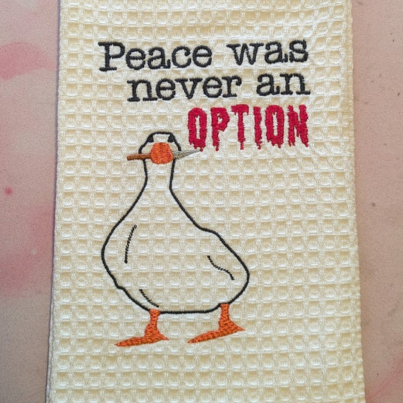 White waffle weave tea towel embroidered with a goose holding a knife in it's beak with the words 
