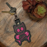 Close‑up of embroidered black cat keychain with pink accents