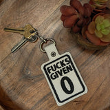 Close‑up of embroidered Fucks Given 0 keychain on white faux leather